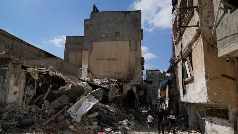 Palestinian refugees walk past the rubble of houses that were...