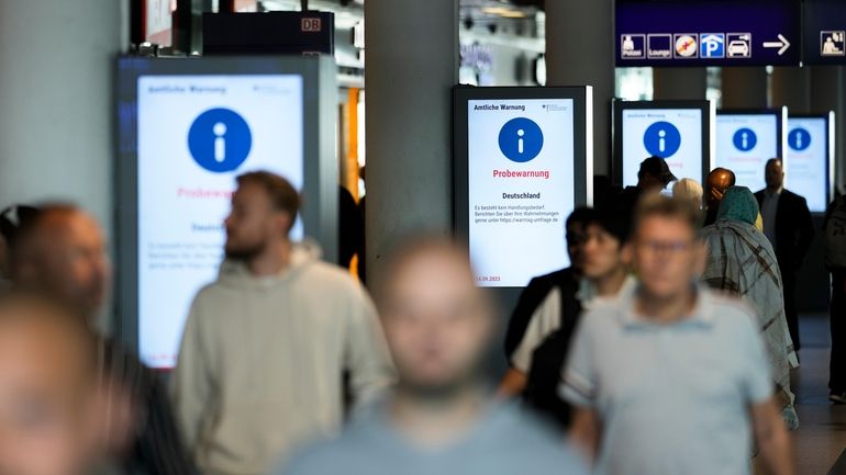 People walk in front of a screens displaying a nation...