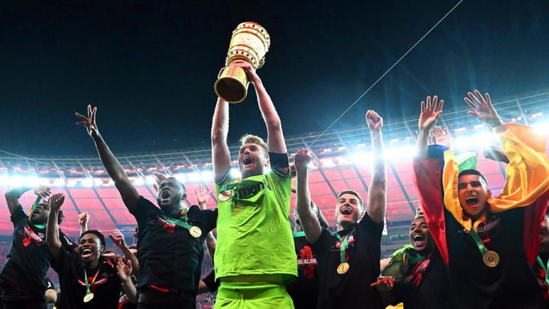Leverkusen goalkeeper Lukas Hradecky holds up the trophy while his...