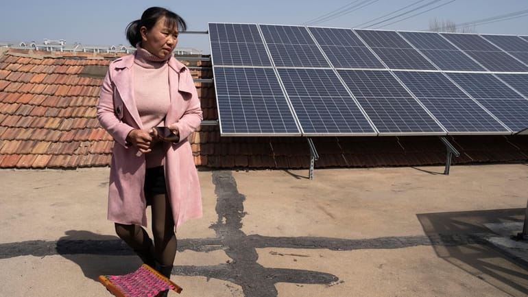 Farmer Shi Mei walks near solar panels on her rooftop...