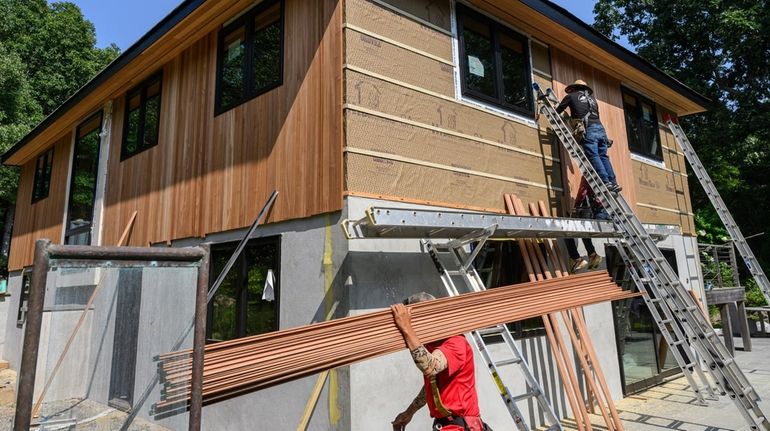 Workers install mahogany siding at a house in Montauk in...