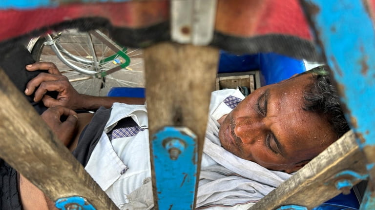 A rickshaw puller sweats while asleep as severe heat grips...