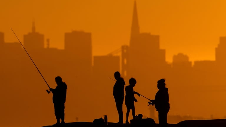 With the San Francisco skyline behind them, people fish off...