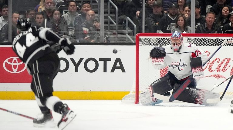 Los Angeles Kings defenseman Mikey Anderson, left, shoots the puck...