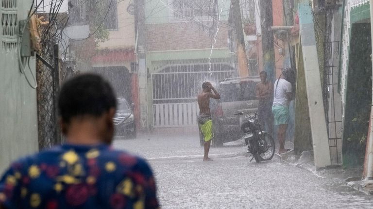 A man stands under a roof drain as the rain...