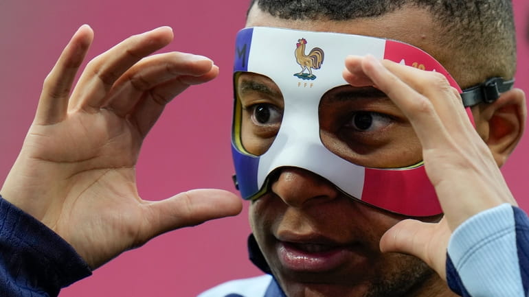 France's Kylian Mbappe adjusts his face mask during a training...