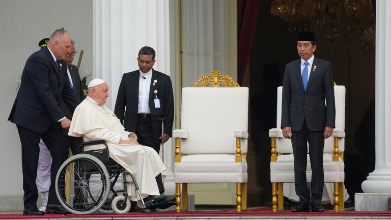 Indonesian President Joko Widodo, right, receives Pope Francis, helped on...