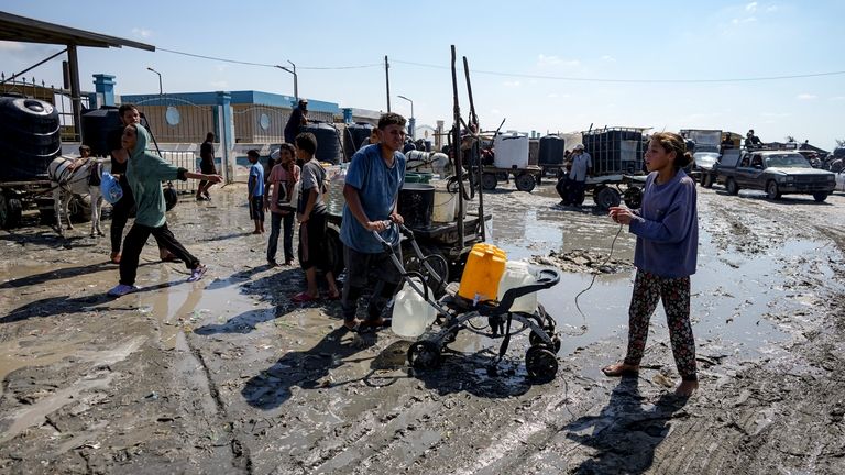 Palestinians gather to fill water jugs at a makeshift tent...