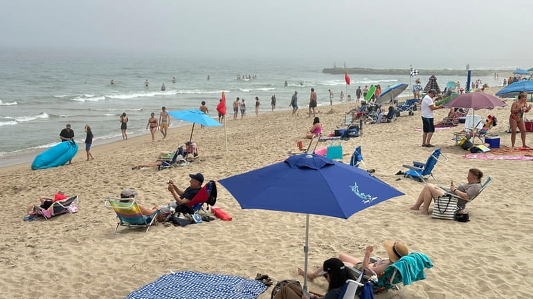 Beachgoers sit on chairs and under umbrellas at Ocean Grove,...