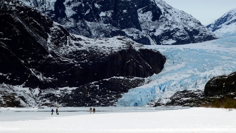 People walk on a frozen Mendenhall Lake, with Mendenhall Glacier...