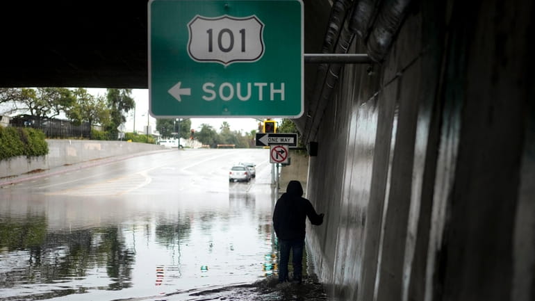 A pedestrian walks under a flooded freeway underpass during a...