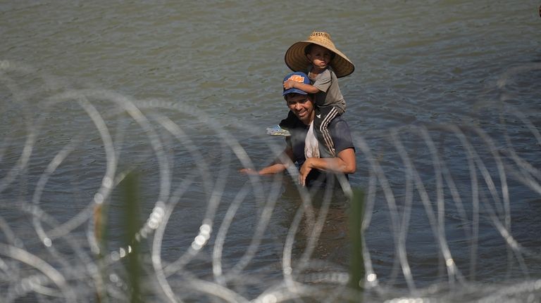 Migrants, one a child, stand in the Rio Grande behind...