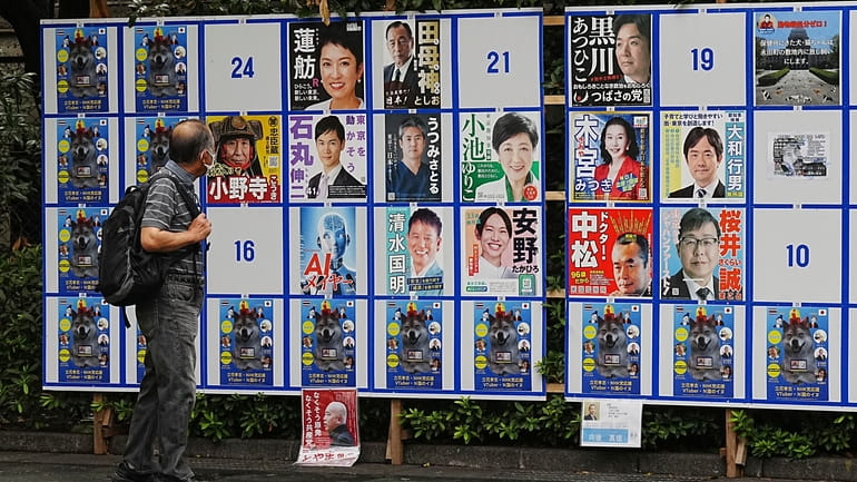 A person looks at an election poster board for Tokyo...