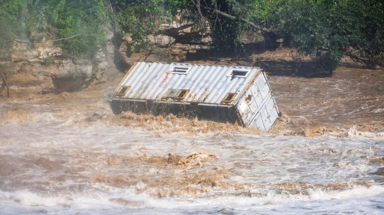 A shipping container barrels down the Blue Earth River, Monday,...