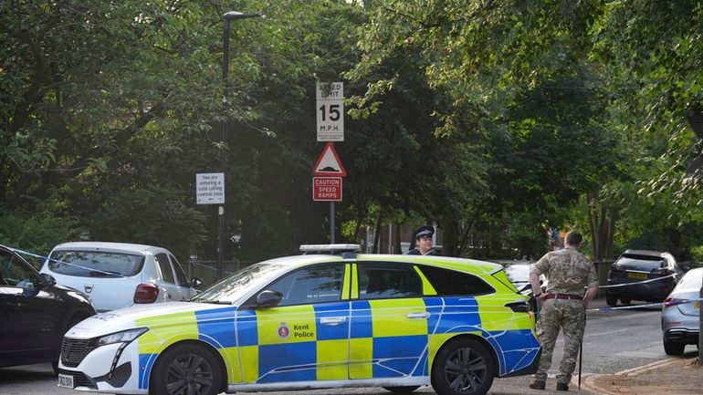 A man in military uniform stands beside a police cordon...