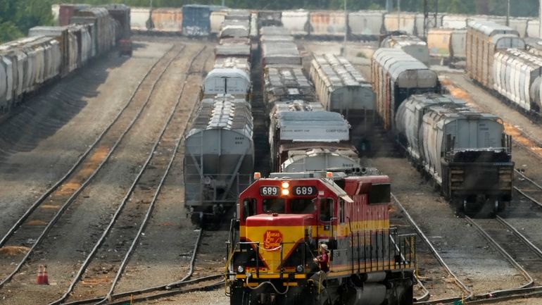 A worker climbs aboard a locomotive at a CPKC rail...