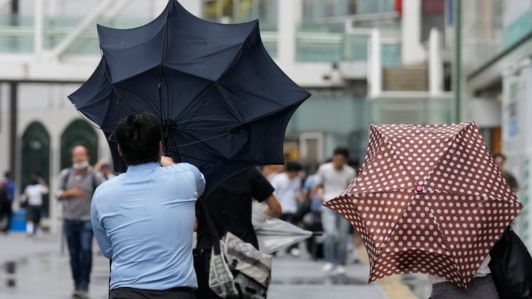 A man with an umbrella struggles against strong wind brought...