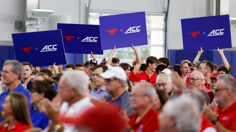 People hold up signs at the announcement of SMU's move...