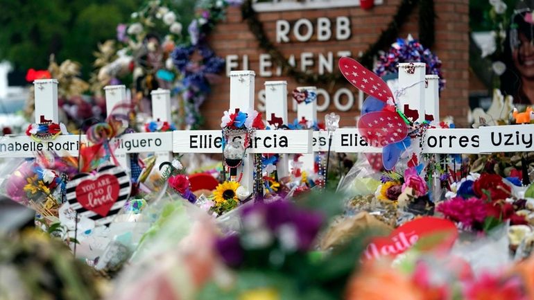 Crosses are surrounded by flowers and other items at a...