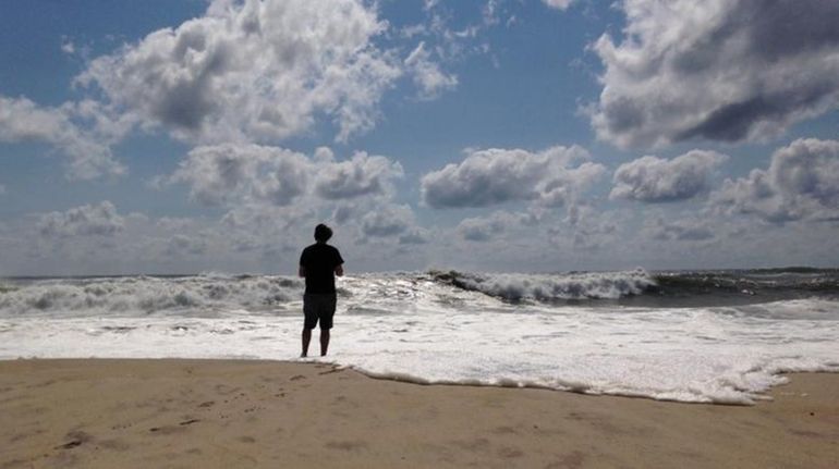 A beachgoer stands at the edge of the water, Sunday,...