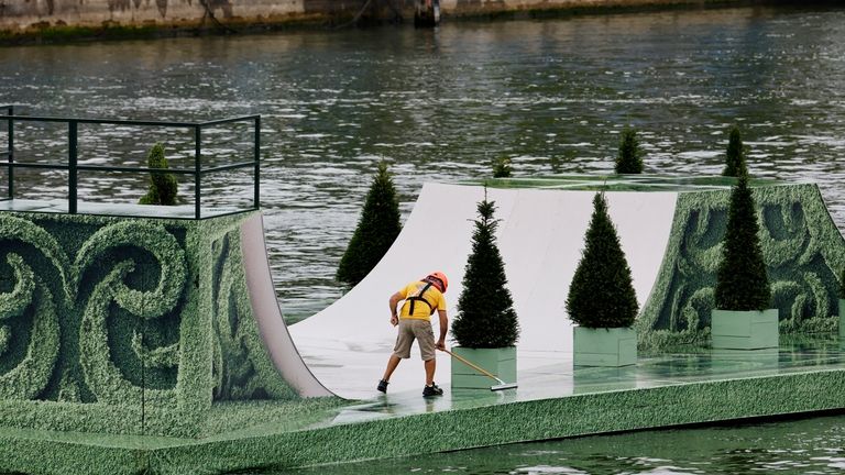 A maintenance worker sweeps water off a skateboard ramp installed...