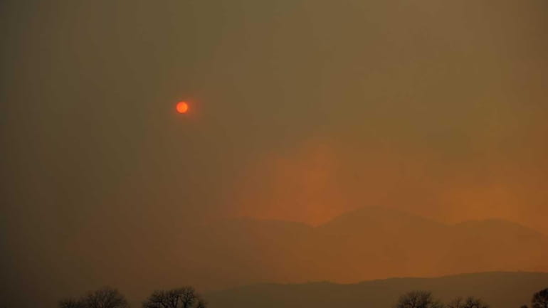 Thick smoke covers the sky as it billows up from...
