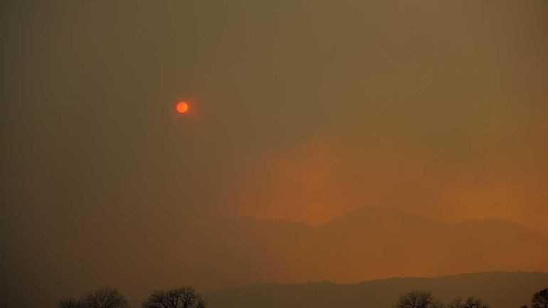 Thick smoke covers the sky as it billows up from...