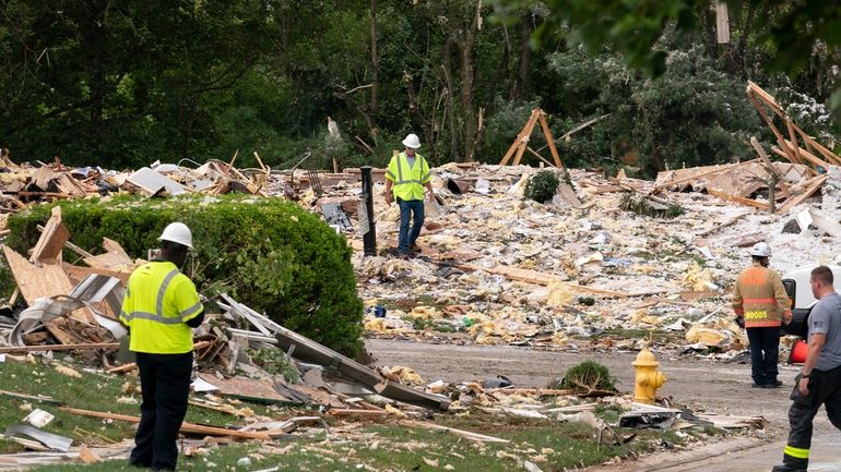 Crew workers remove the debris after a house exploded in...