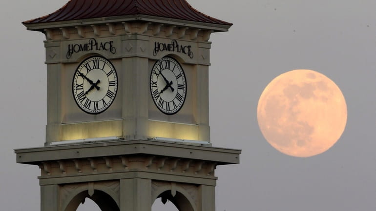 The moon rises behind the Home Place clock tower in...