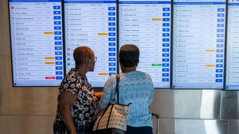 Passengers check a flight board at Kennedy Airport on Friday after...