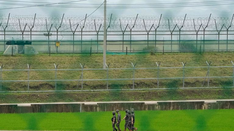 South Korean army soldiers pass by the barbed-wire fence in...