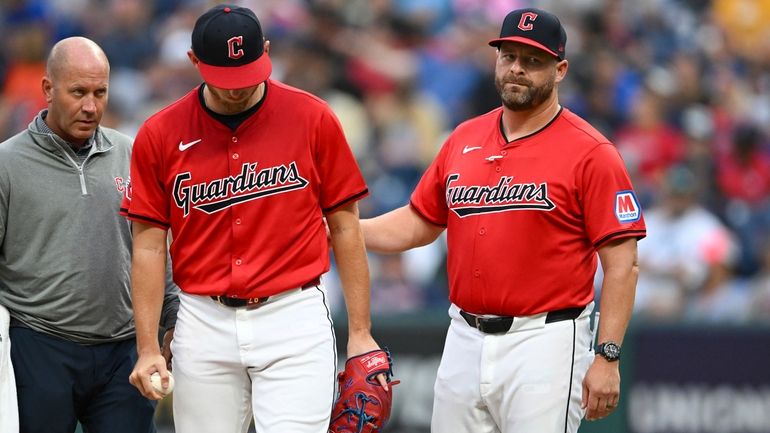 Cleveland Guardians manager Stephen Vogt, right, helps starting pitcher Tanner...