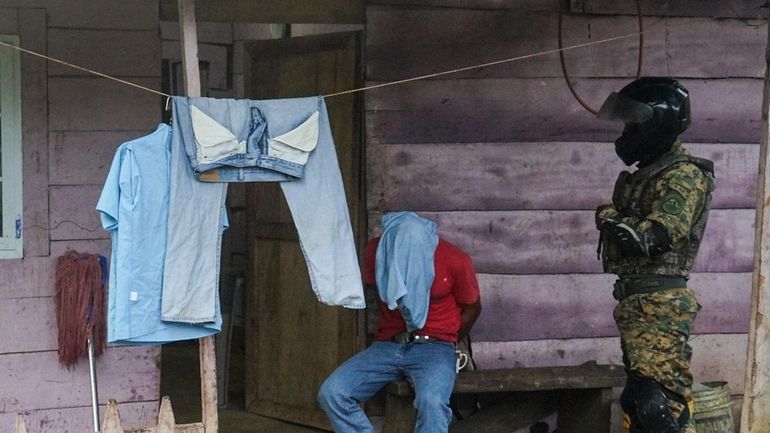 A detainee sits with their hands cuffed by a member...