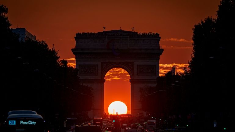 The setting sun, framed by the Arc de Triomphe, illuminates...