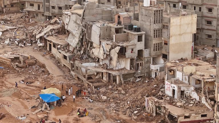 Rescuers and relatives sit in front of collapsed buildings after...