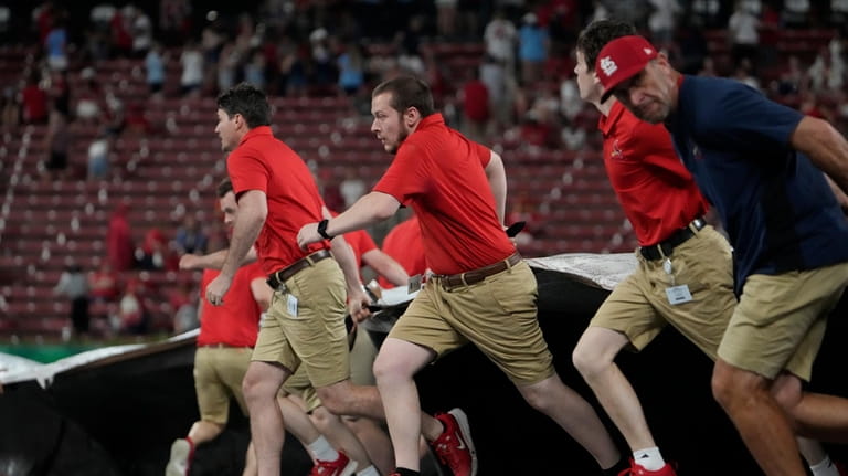 Members of the Busch Stadium grounds crew rush to unfurl...