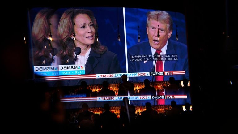 Reflected in a mirror, people watch the presidential debate between...