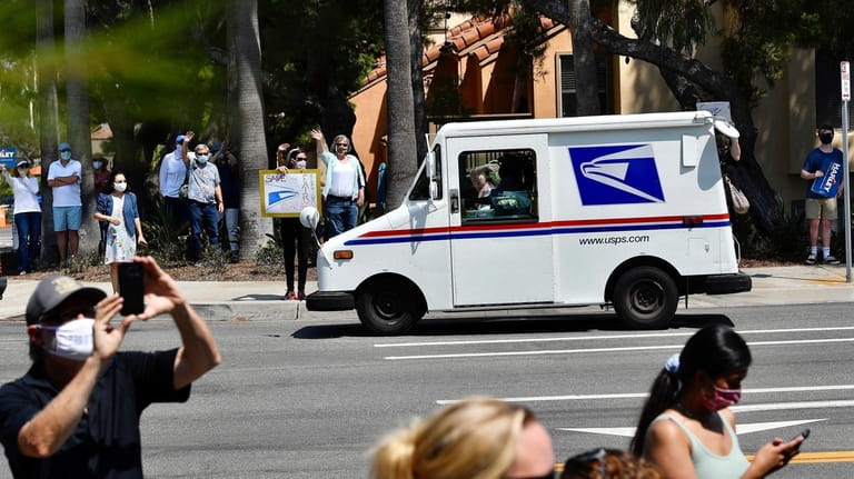 A postal carrier drives past protesters during a rally against...