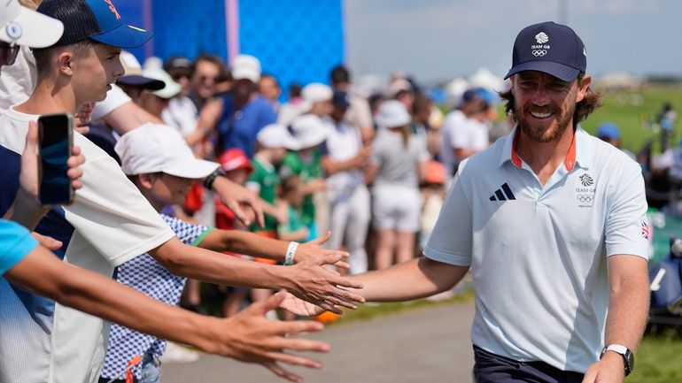 Tommy Fleetwood, of Great Britain, taps hands with fans as...