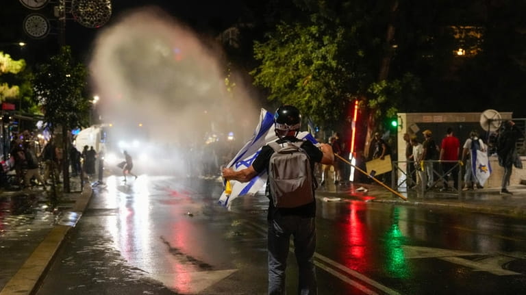 Israeli police use a water cannon to disperse demonstrators blocking...