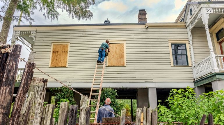 The windows of a raised historic house are boarded up...