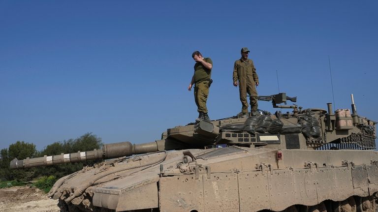 Israeli soldiers stand on their tank in a staging area...