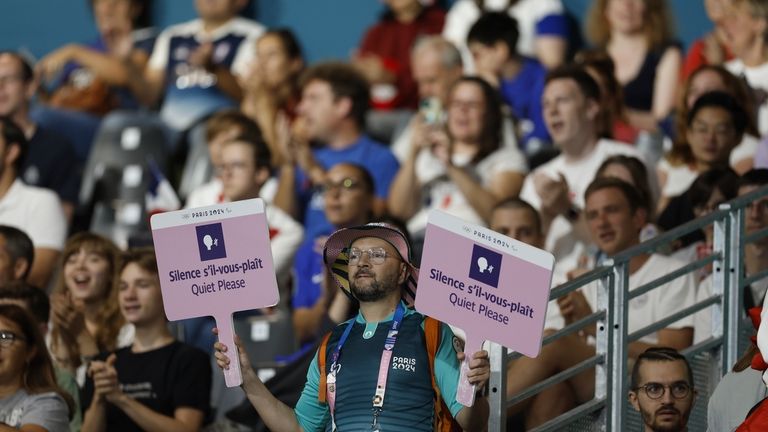 A volunteer for the Paralympic Games holds two signs reading...