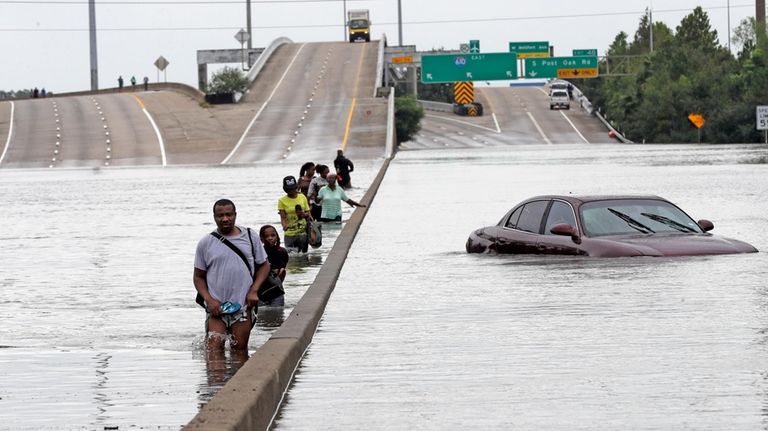 Evacuees wade down a flooded section of Interstate 610 as...