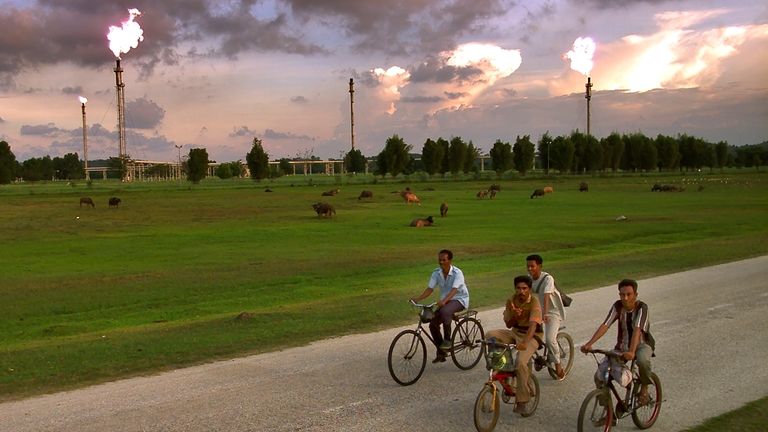 FILE- Acehnese men bicycle to work past an Exxon Mobil...