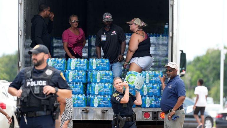 A Houston police officer carries a case of water to...