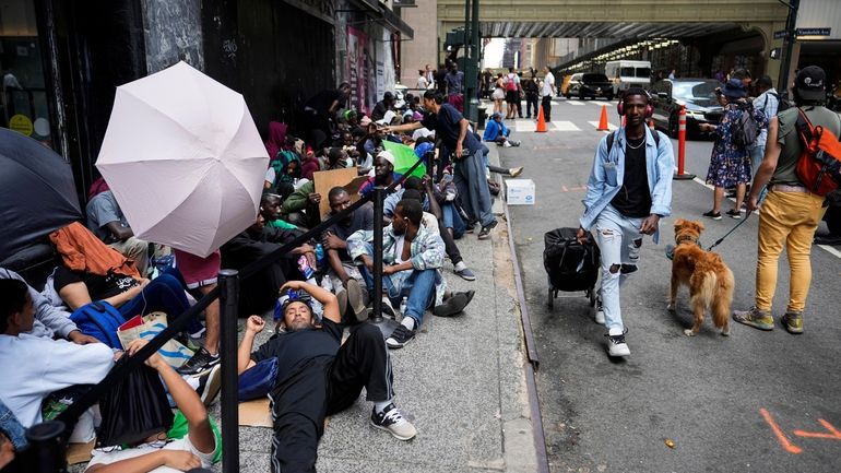 Migrants sit in line outside The Roosevelt Hotel, which is being...