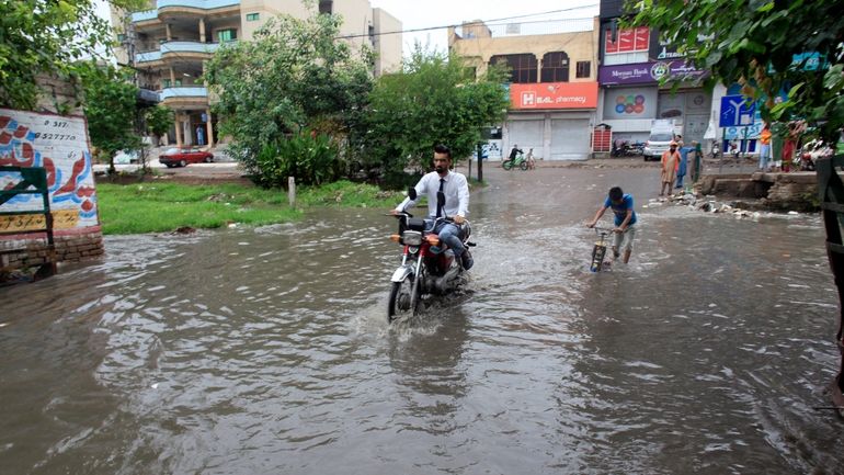 A motorcyclist drive through a flooded road caused by heavy...