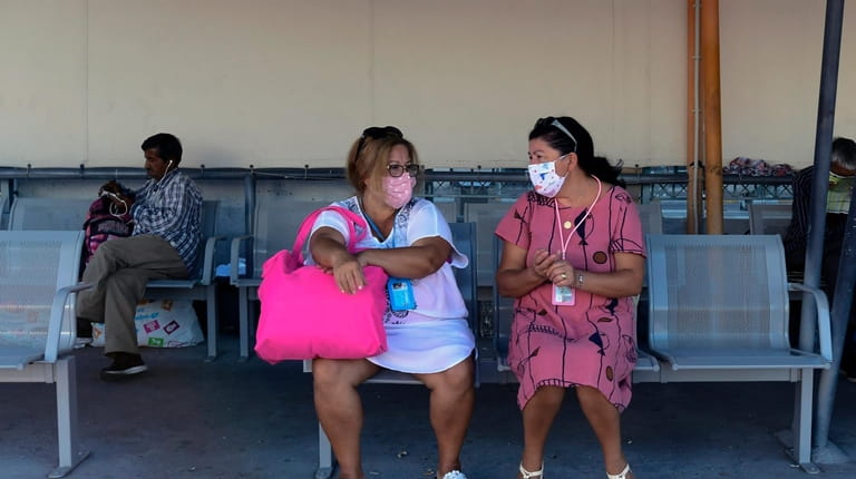 Women wearing face masks sit on a bench at the...