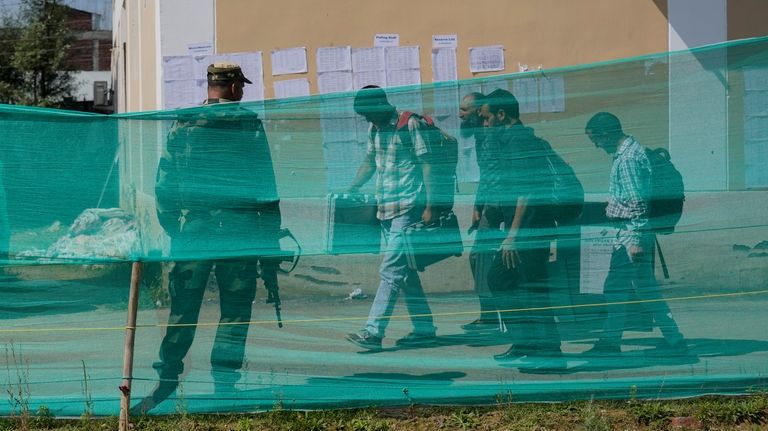 Indian paramilitary soldier guard as polling officials carry electronic voting...